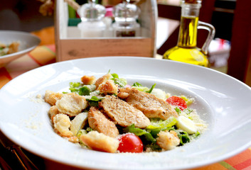Caesar salad with croutons, quail eggs, cherry tomatoes and grilled chicken in a white plate on a table in a restaurant