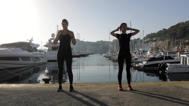 Young women doing exercises at sea port. Fit attractive caucasian girls warm up clapping muscles of the body