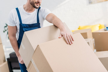 cropped view of mover in uniform transporting cardboard boxes in apartment