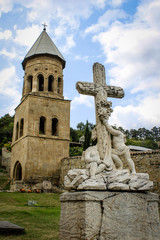 Fototapeta na wymiar Church tower and tombstone with a cross and two headless angels. Religion, Georgia, Mtskheta. Temple. Monument, statue. Architecture