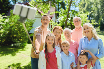 generation and people concept - happy family taking picture with smartphone and selfie stick in summer garden