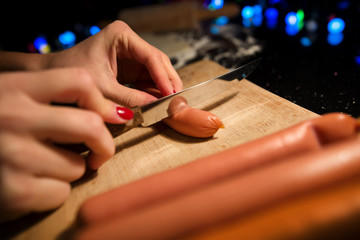 Preparing tanned wiener sausages in pizza dough. Cutting sausages on wooden board before baking. Dark background in kitchen. Making snacks for family and friends
