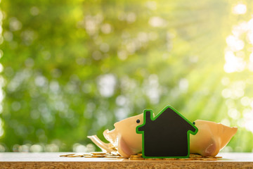 Wooden home with blackboard and broken a piggy bank and gold coin on bokeh in the public park, Loan or saving money for buy a house and real estate concept