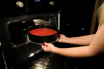 Woman is cooking in kitchen, baking a red velvet cake. Taking out or putting a biscuit tray filled...
