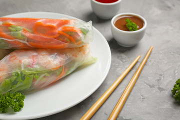 Plate with tasty spring rolls on grey background