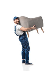 handsome mover in uniform looking at camera while carrying grey armchair isolated on white