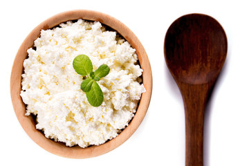 homemade cottage cheese in a wooden bowl, mint, wooden spoon lie on a white background