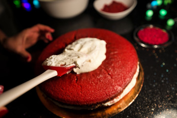 Woman spreading whipped cream over freshly made cake, creating ornaments and decorating dessert. Beautiful home made red velvet cake decorated with whipped cream and raspberry crumbs