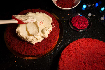 Woman spreading whipped cream over freshly made cake, creating ornaments and decorating dessert. Beautiful home made red velvet cake decorated with whipped cream and raspberry crumbs