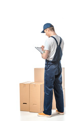 back view of mover in uniform writing in clipboard near cardboard boxes isolated on white