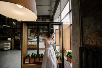 Model posing in a white long wedding dress indoors by the window. Advertising of wedding dresses
