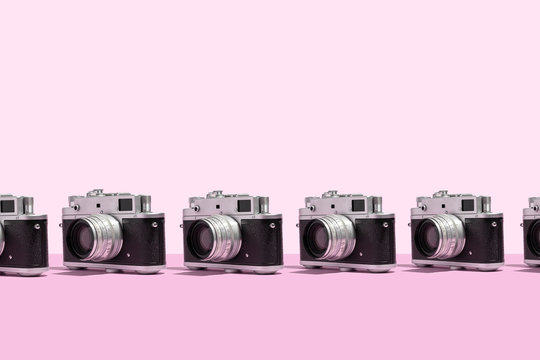 Photo cameras organized in a row over pink background