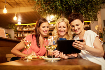 leisure, technology and lifestyle concept - happy women with tablet pc computer at wine bar or...