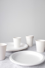 Fototapeta na wymiar set of empty reusable disposable eco-friendly plates, cups, utensils on light white and grey concrete table top on white wall blurred background with copy space. Top view. 