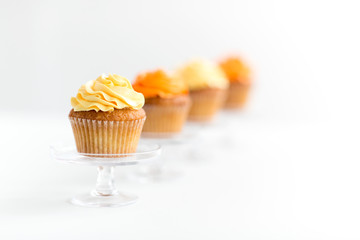 food, pastry and sweets concept - cupcakes with buttercream frosting on glass confectionery stand over white background