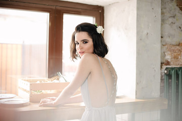 Model posing in a white long wedding dress indoors by the window. Advertising of wedding dresses