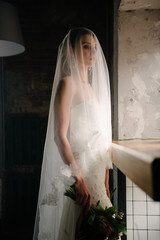 Model posing in a white long wedding dress indoors by the window. Advertising of wedding dresses