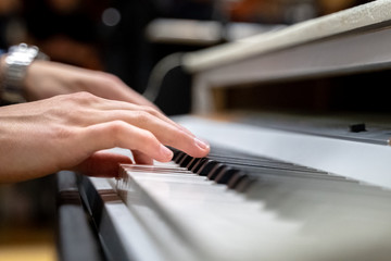 Male hands with long fingers playing music on keyboard with white and black keys of a piano