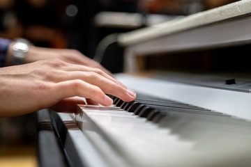 Male hands with long fingers playing music on keyboard with white and black keys of a piano