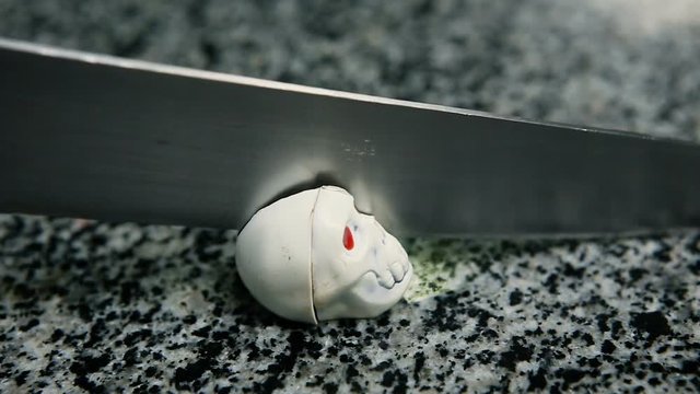 closeup chocolate candy in skeleton skull shape with red eyes cut in half by knife on kitchen table