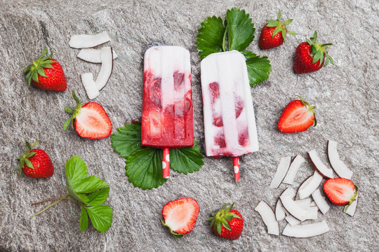 Homemade strawberry coconut ice lollies with fresh strawberries and coconut slices on granite