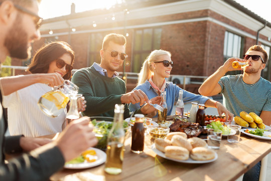 leisure and people concept - happy friends eating and drinking at barbecue party on rooftop
