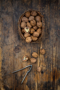 Wicker basket of walnuts and nutcracker on wood