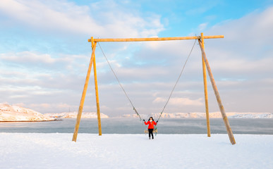 Fototapeta premium Asian woman sitting on huge swing on Arctic beach