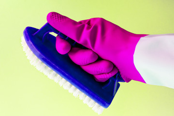 Hand in pink rubber latex glove holding a brush for cleaning surfaces, carpet, bathroom on yellow background, spring cleaning, space cleaning