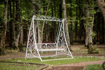 metal white swing on the background of a garden plot, park or forest
