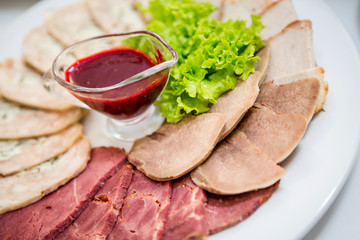 white plate with sliced meat, fresh herbs and red sauce in a glass saucepan