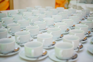 lot of tea cups and saucers on the table covered with a white tablecloth