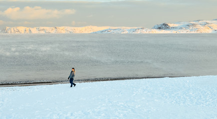 Fototapeta na wymiar Single young Chinese male walking beach on snowy beach by Arctic ocean, in Teriberka, Russia