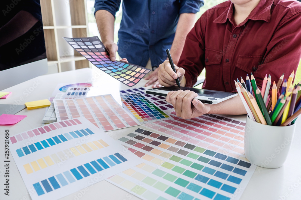 Poster Two colleague creative graphic designer working on color selection and color swatches, drawing on graphics tablet at workplace with work tools and accessories