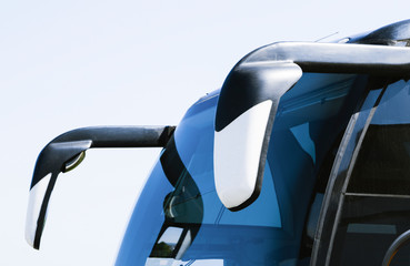 The front part of the tourist bus on the background of the village.  The image shows a windshield and two mirrors.