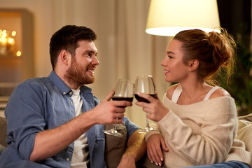 leisure, celebration and valentines day concept - happy couple drinking red wine at home in evening