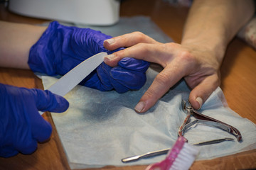A manicurist grinds a nail with a nail file for a manicure.