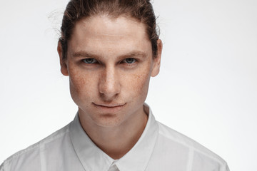Portrait of a handsome long-haired man with drawn hair and freckles dressed in a white shirt