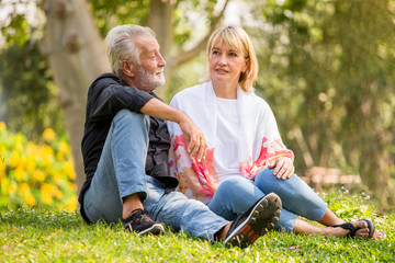 Fototapeta premium Happy senior couple relaxing at park together in morning time. old people sitting on grass in the autumn park . Elderly resting .mature relationships. family