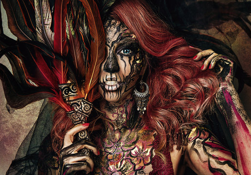 Close up portrait of sexy beautiful witch with Halloween makeup. Beautiful redhead hair. Professional creative face painting. Feathers on face