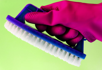 A hand in a rubber glove holds the dishwashing brush on pastel background. The concept of bright spring, spring cleaning.