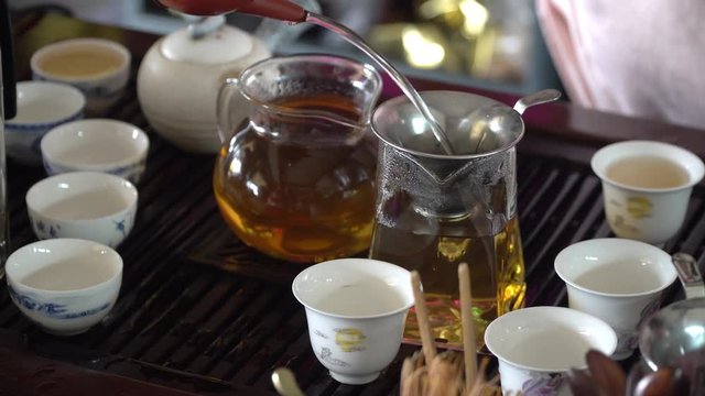 4k Video footage close up of woman hand take the teapot and pouring the hot tea into the glass serving jar with ceramic tea cup set on the table. Chinese tea ceremony. 