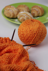 Horizontal photo of the knitting process of orange yarn. Behind are croissants, dessert. Blur effect