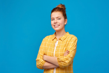 people concept - smiling red haired teenage girl in checkered shirt with crossed arms over bright...