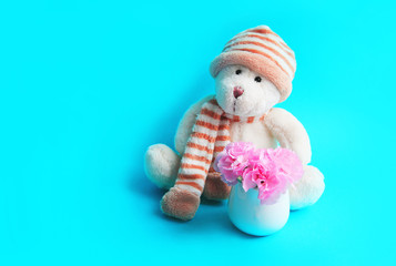 teddy bear in a hat and balls next to a bouquet of pink carnations in a vase on a blue background concept of holiday and activities.