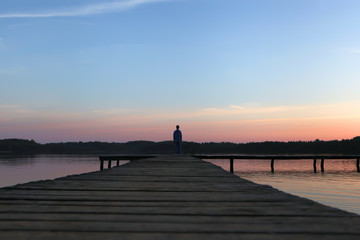 Wooded bridge over the river with younger silouette at the sunset time