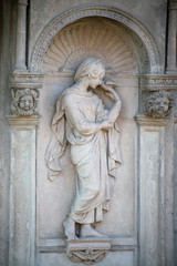 Fototapeta na wymiar Relief Statue aus Stein einer jungen Frau mit einem Vogel in der Hand und zwei Putten auf dem Dorotheenstädtischen Friedhof in Berlin