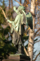 Grüne Bronzeplastik eines Engel auf Podest von hinten (Seitenansicht) auf dem Dorotheenstädtischen Friedhof in Berlin