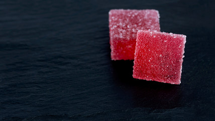 wo pieces of red marmalade lies on a stone black background.
