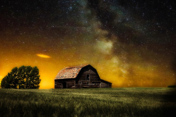 An old wooden barn in a wheat field under a milky way sky in a countryside nighttime landscape